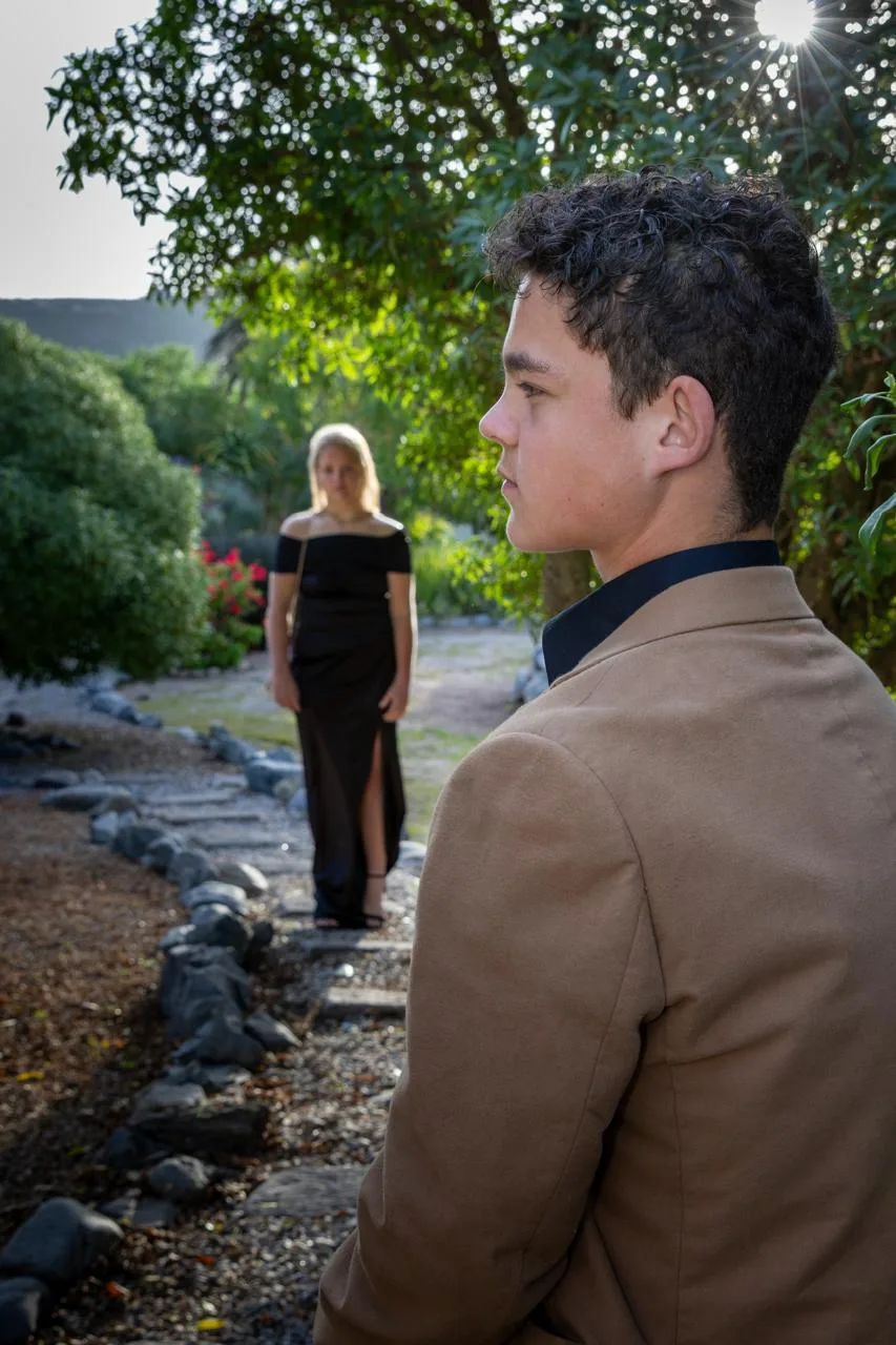 A young man in a tan jacket looking back at his date on a garden path